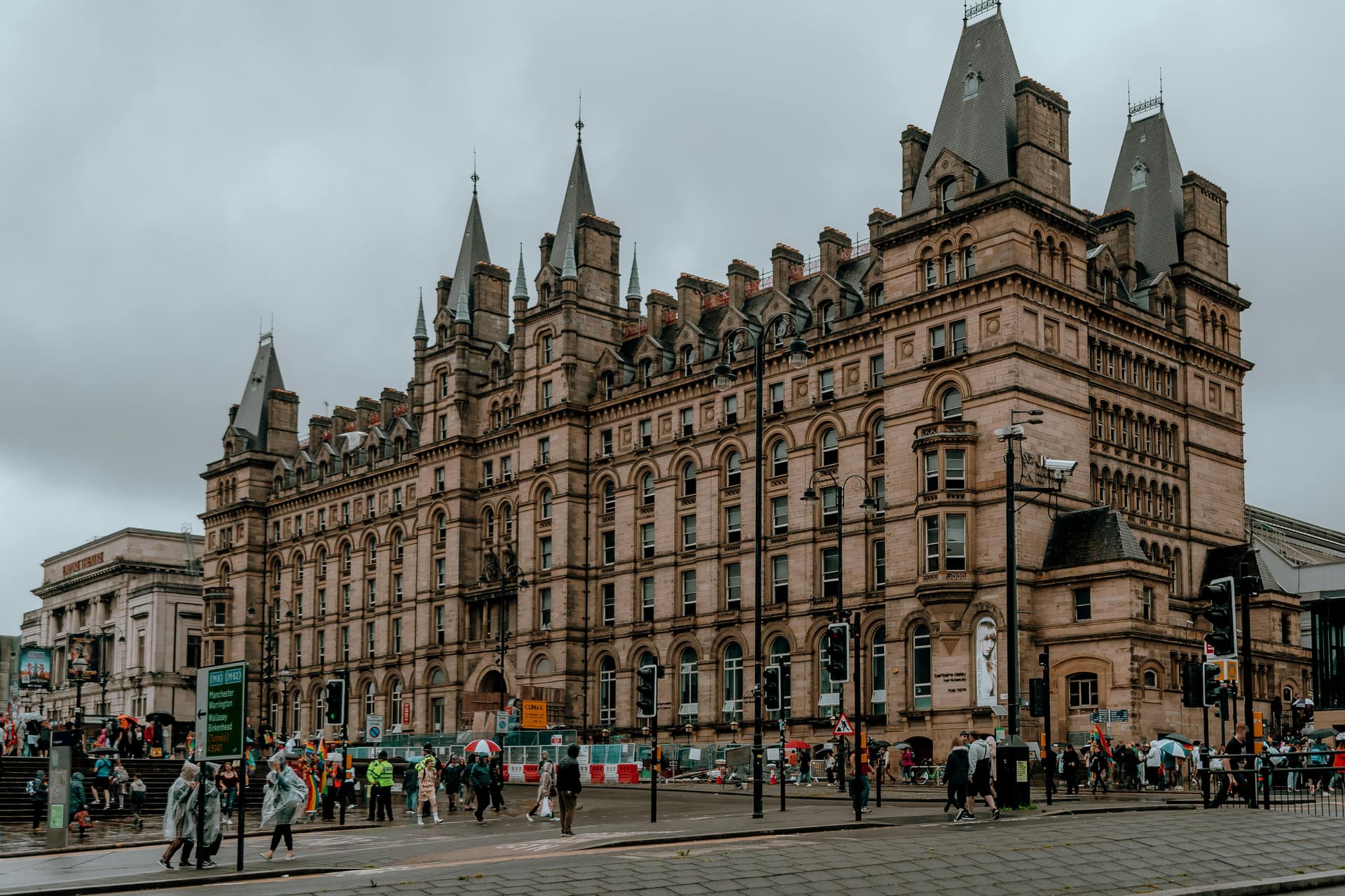 A large historical building with spires, surrounded by people and a cloudy sky.